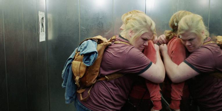 Zu sehen sind zwei Personen die sich in einem Fahrstuhl umarmen.